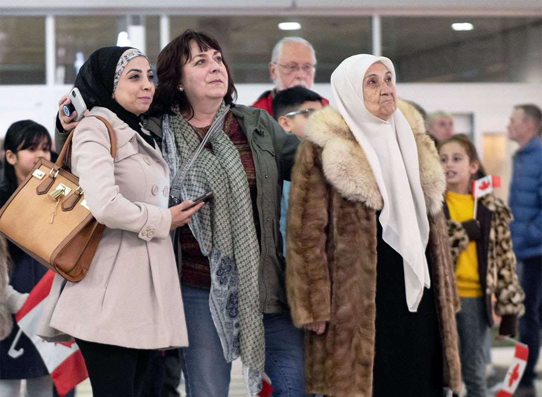 Fatema, Shelley and Abdulnaser's sister, Souhair stand together, looking toward the escalator at Regina International Airport.