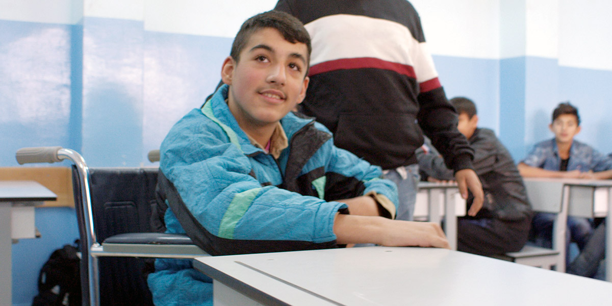 Abdulrahman, who uses a wheelchair, sits smiling at his desk.