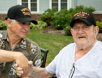 An older man with a Vietnam Vet hat sits next to an elderly man with a World War 2 Vet hat