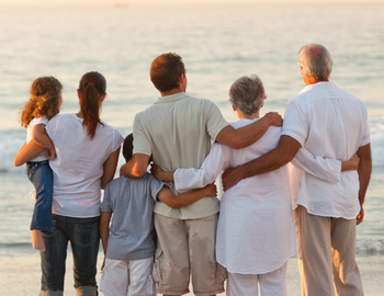 Multigenerational family stands back to the camera looking out the ocean