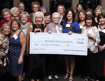 A large smiling group of women holding a large check for Hospice House.