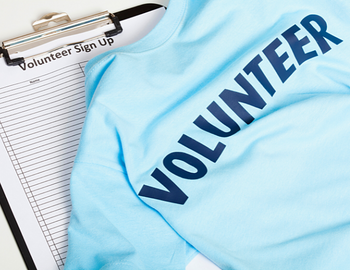 A blue shirt with the words "VOLUNTEER" in all caps laying on top of a sign up form & clipboard