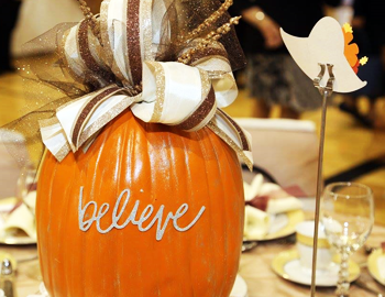 An orange pumpkin with a large fancy ribbon in the centerpiece of a table. 