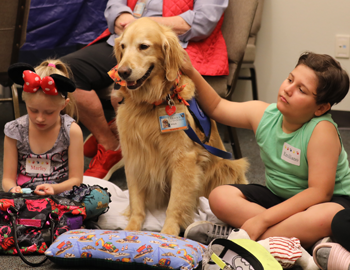 Two children sit between a therapy golden retriever 