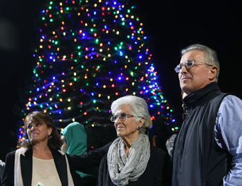 Three people stand in front of a tree covered in lights