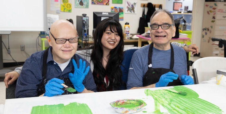 Two male artists and a female employee of Hope sit together and work on a painting