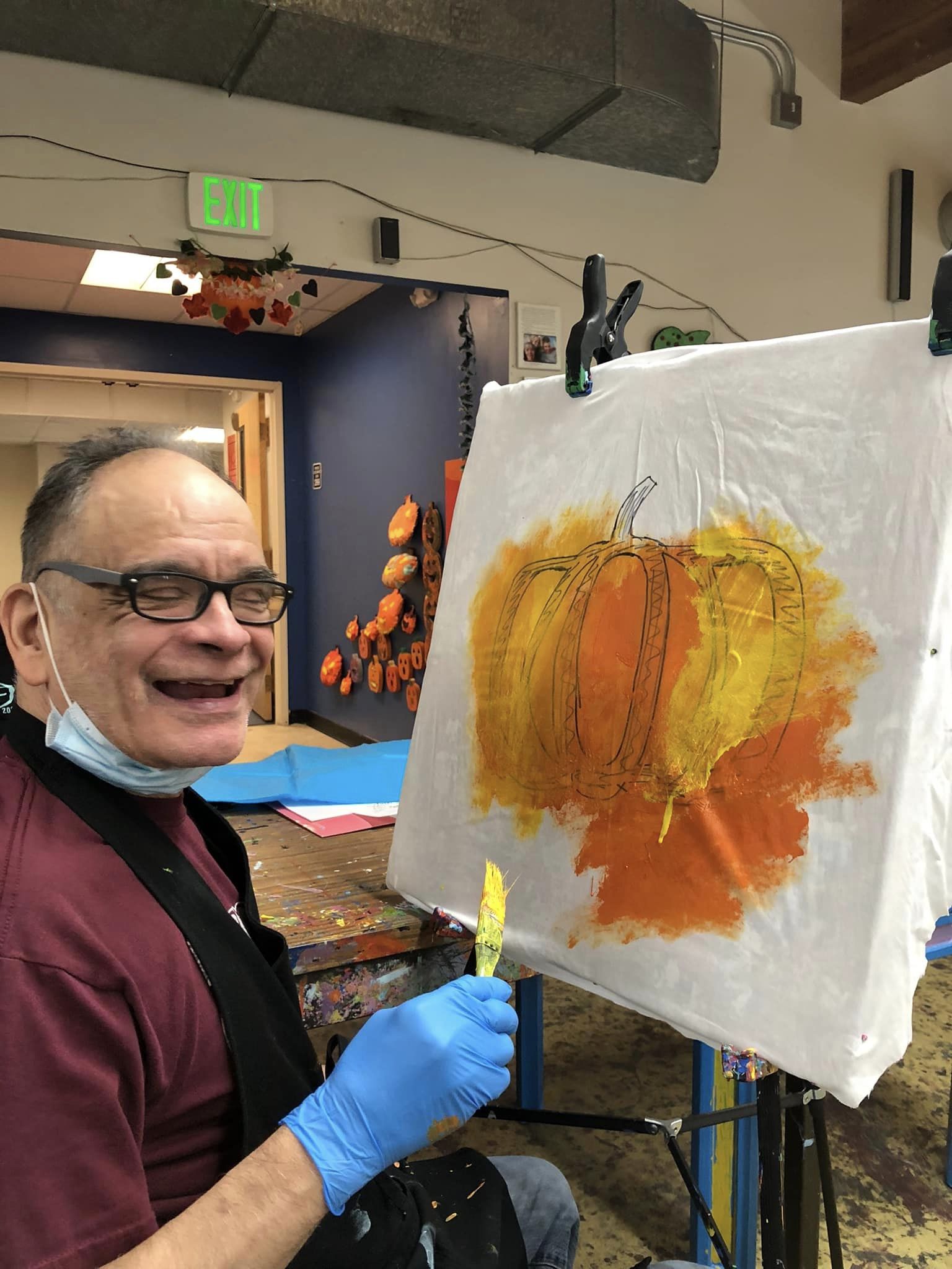 A man smiles while painting a pumpkin on a canvas