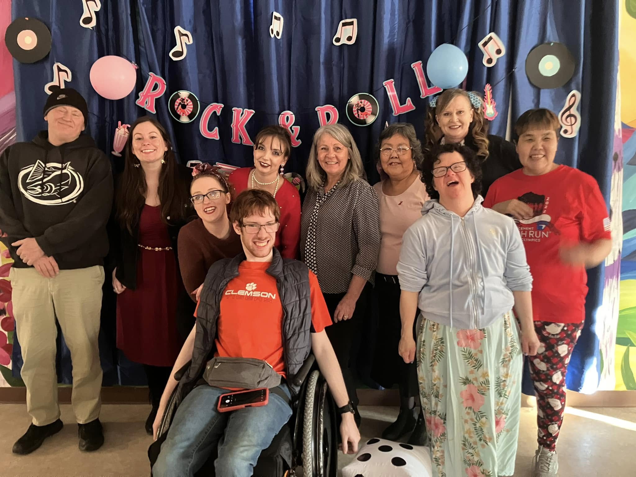 A man smiles while holding a fish he just caught in the river behind him.