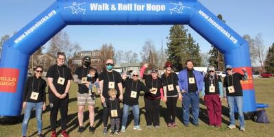 A team of 12 of Hope's staff and family members stand in front of an inflatable 'Walk and Roll for Hope' race arch.