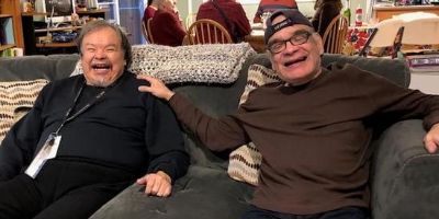 Two adult brothers who receive supports from Hope sit side-by-side on a couch. One has his hand on the other's shoulder, and both are smiling.