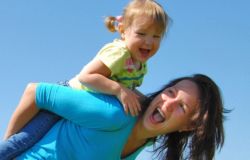 A woman in a blue shirt holds her foster daughter on her back playfully, and both are smiling.