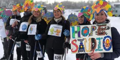 A group of Hope Studios’ female DSPs are dressed in costume and wearing race bibs. One woman holds a sign that says 'HOPE STUDIO.' They won the “Best Costume” award at the judged costume parade at Ski for Women in February 2023.