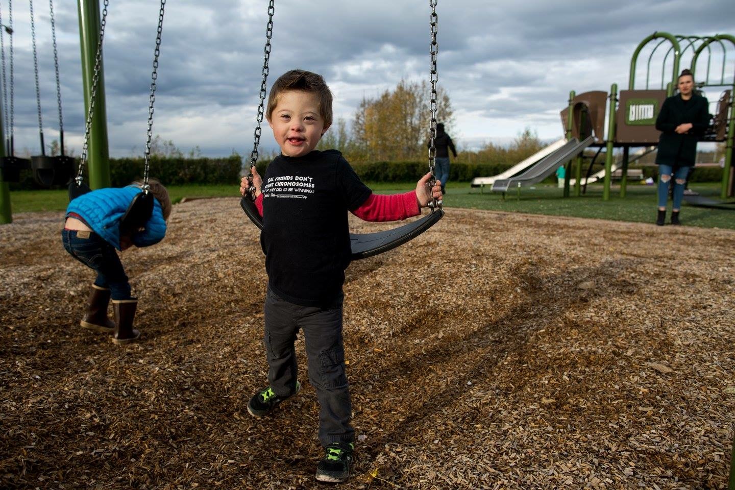 Two children are at a playground swinging on the swings