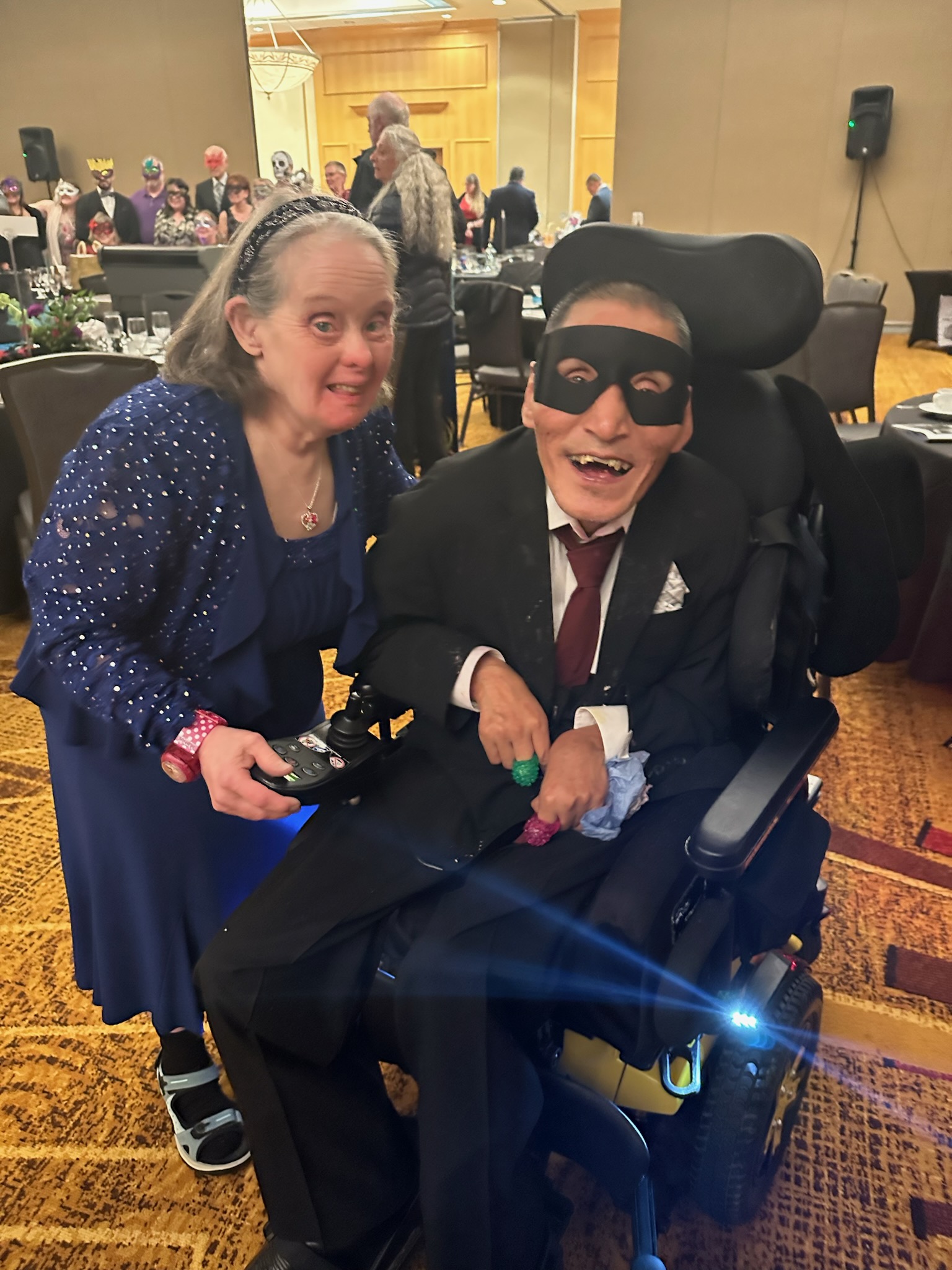 A woman dressed in an elegant blue dress and a man wearing a suit and black eye mask attend Hope's annual auction