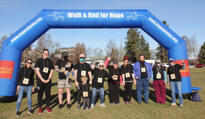 Ten adults and two children stand in front of a 'Walk for Hope' inflatable race arch