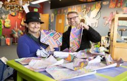 A man and woman in Hope's Art Studio holding up artwork and smiling.