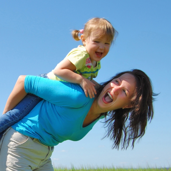 A woman in a blue shirt holds her foster daughter on her back playfully, and both are smiling.