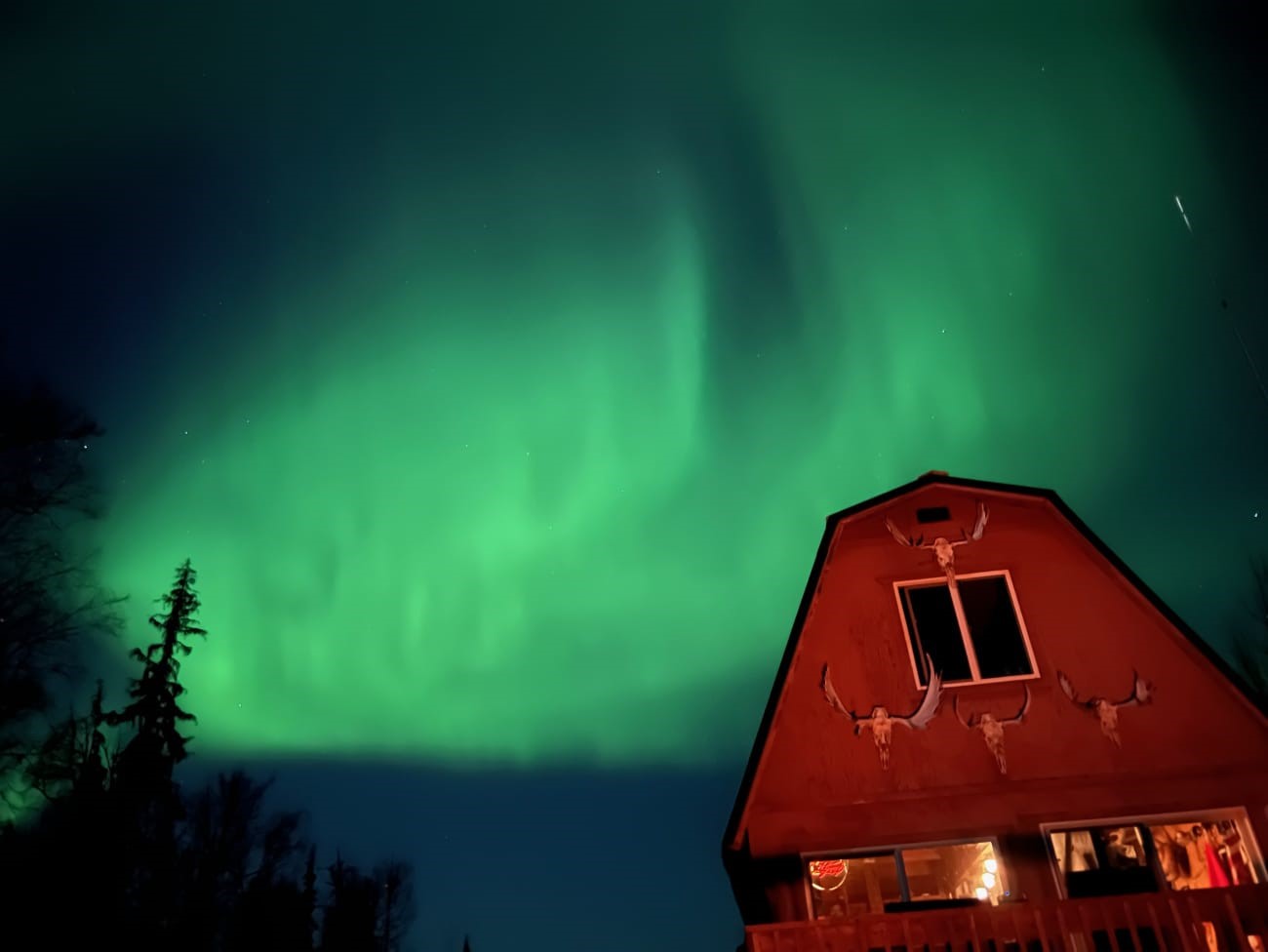 A red barn in front of the Aurora Borealis lighting up the night sky.