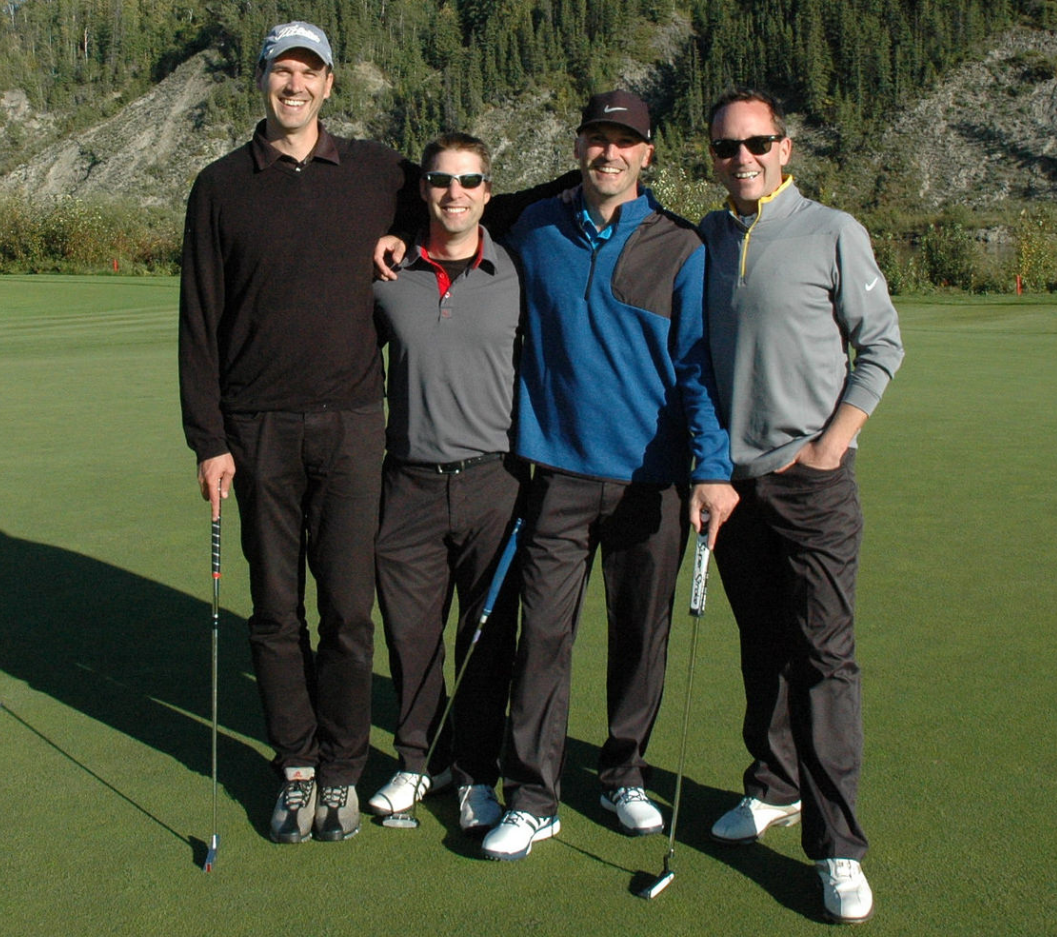 four people holding golf clubs and posing on the golfing green