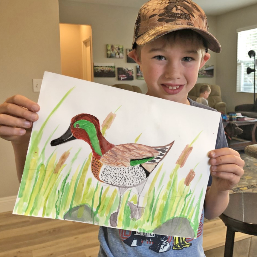 A boy holds up his watercolor of a green-winged teal.