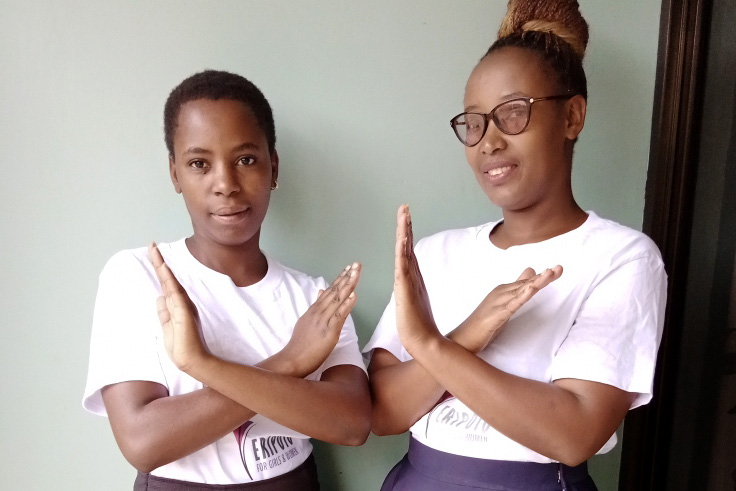 Two Tanzanian women cross their arms in front of their chests to signal ’Break the Bias”