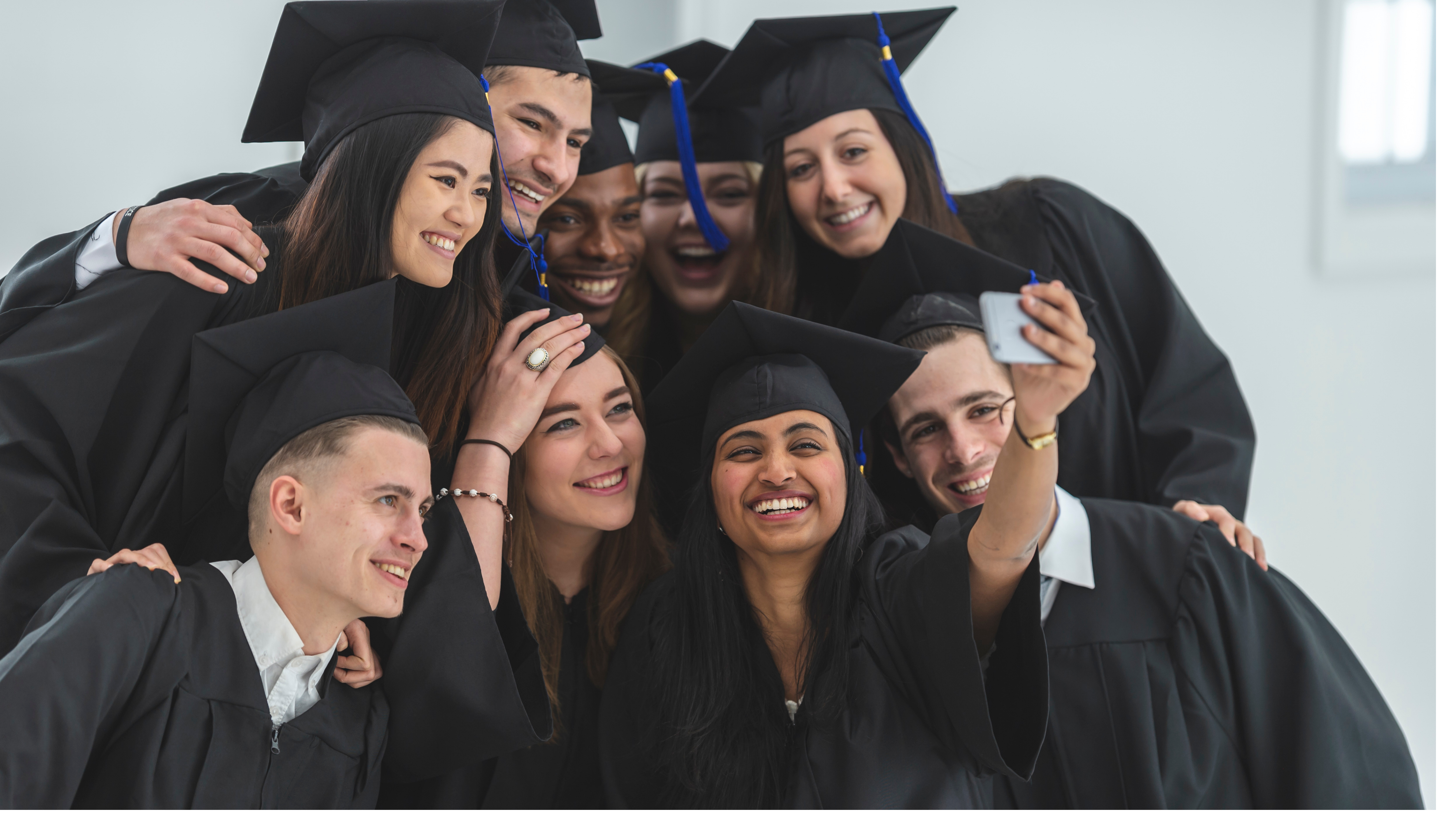 A diverse group of nine students in graduation gowns and hats taking a group photo of themselves
