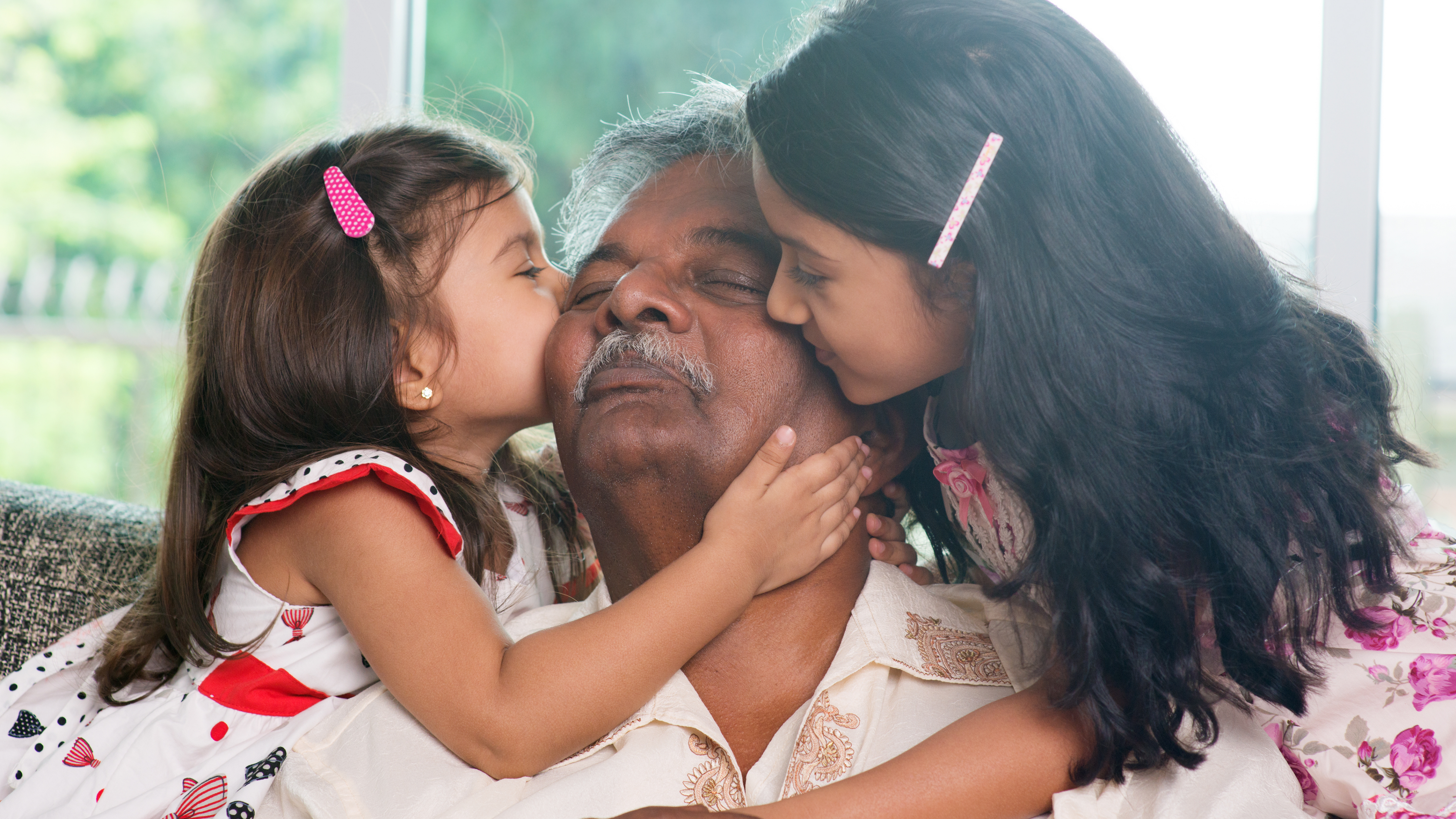 Two young girls cuddle and kiss their grandfather who looks delighted by their affection.