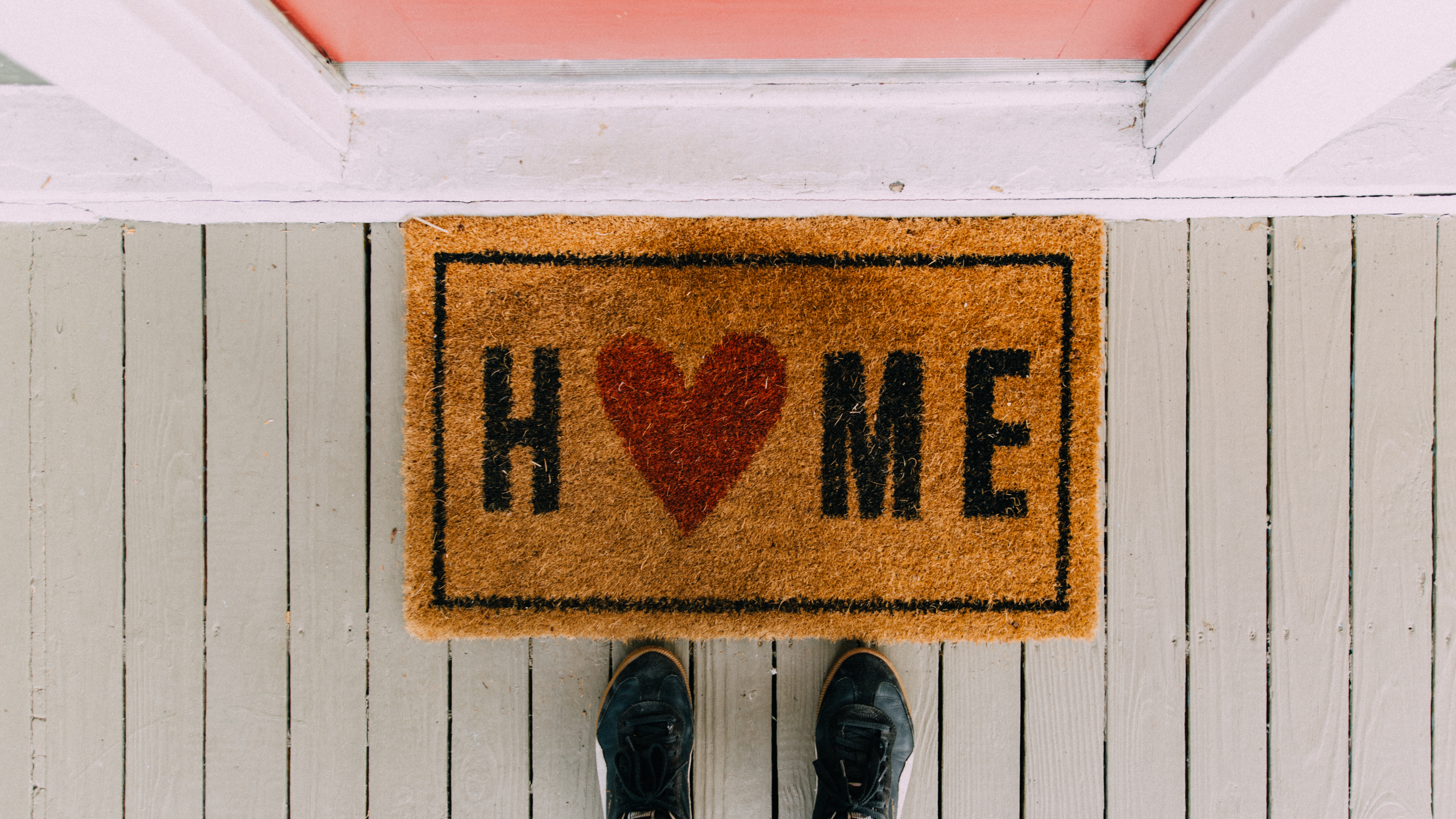 A floor mat in front of a door with the word "Home" in it but the "O" in home is replace with a red heart