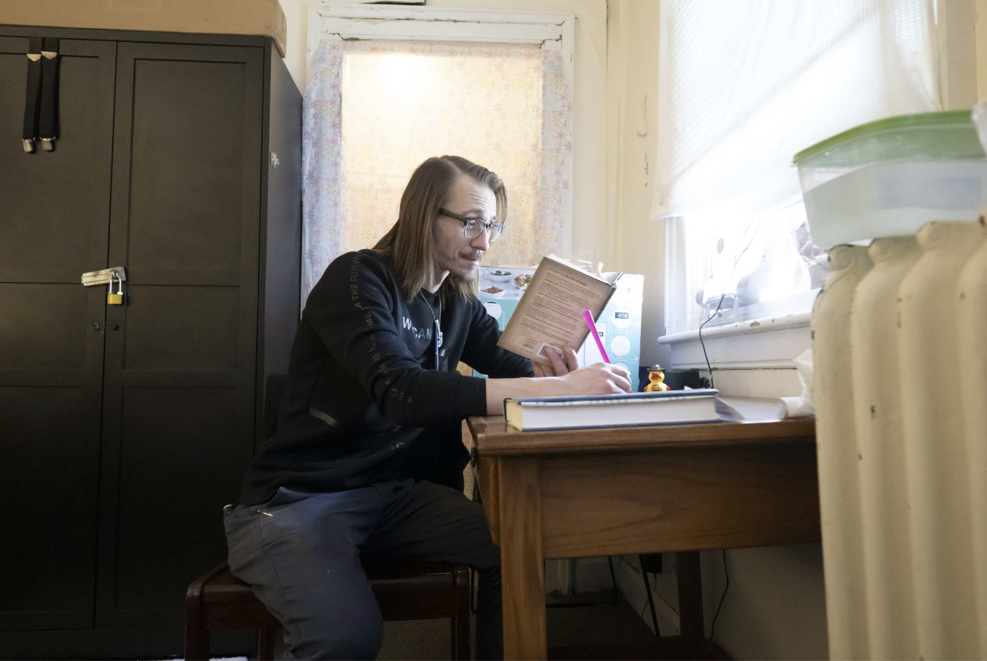 A person reading and writing at a desk beside a window