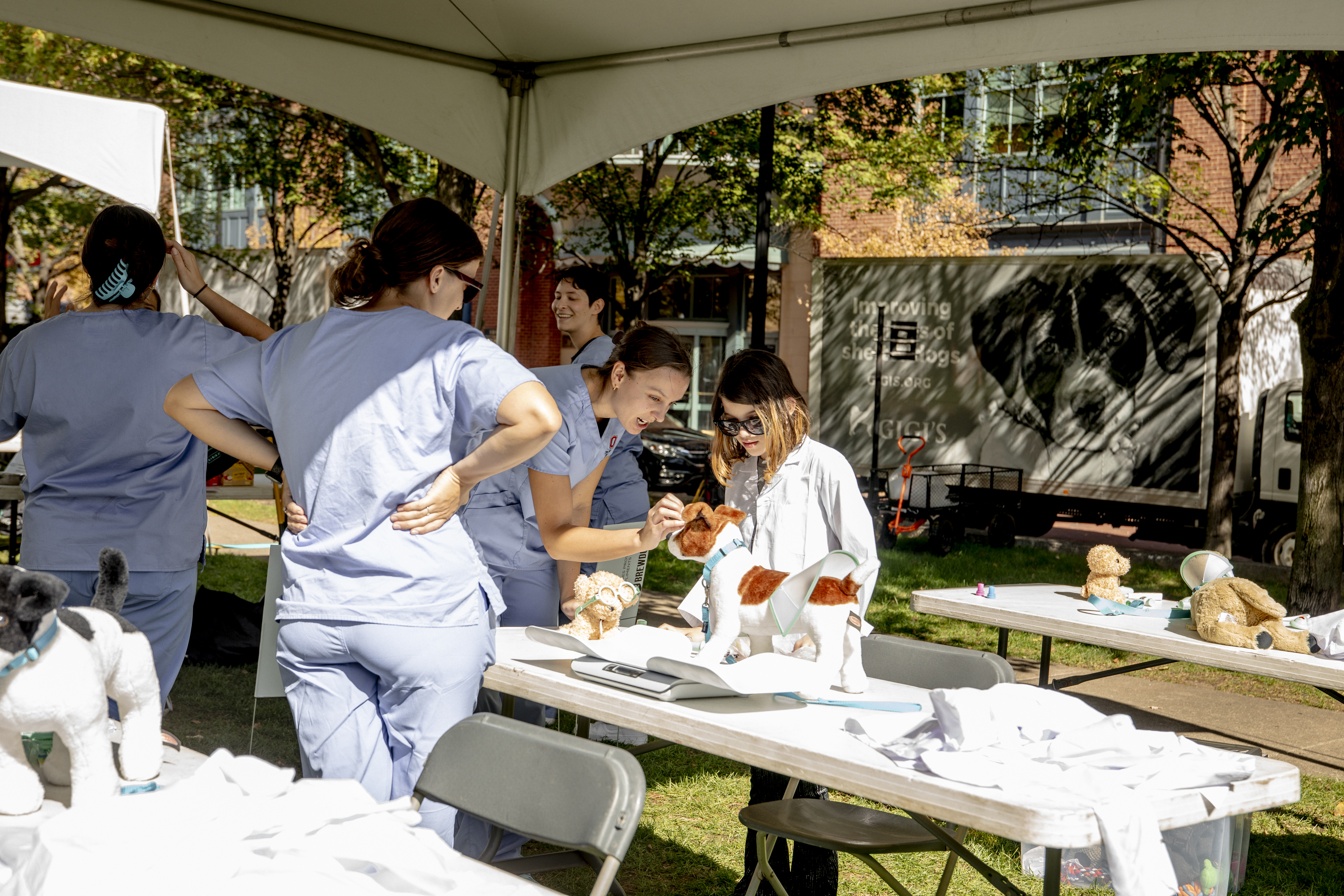 A child in a lab coat examining a stuffed dog with veterinary students